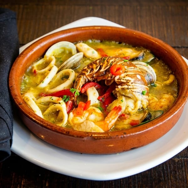 Seafood stew with lobster, shrimp, squid, and clams in a terracotta bowl on a wooden table.